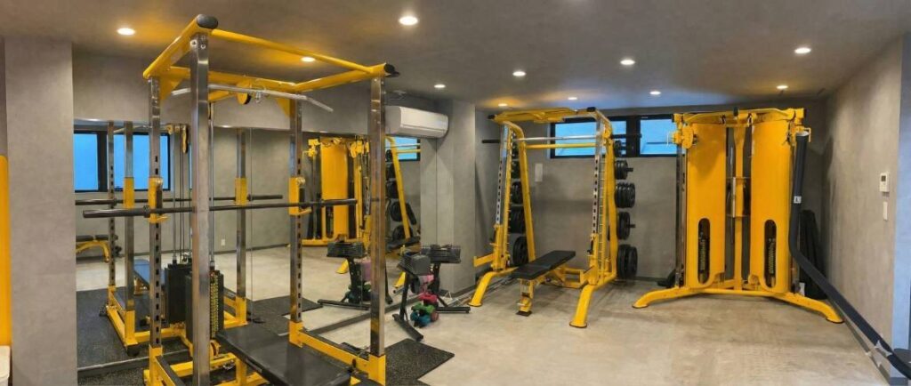 コンクリート打ちっぱなしの壁と鮮やかな黄色のフレームのマシンで統一された、habitのスタイリッシュな完全個室トレーニングルーム。パワーラック、スミスマシン、ケーブルマシンなどが完備され、大きな鏡が設置された清潔感のある空間。